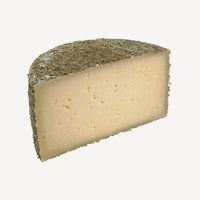 Una mitad de queso revela la consistencia perfecta y la integración armoniosa de finas hierbas, invitando a una experiencia de sabor única.